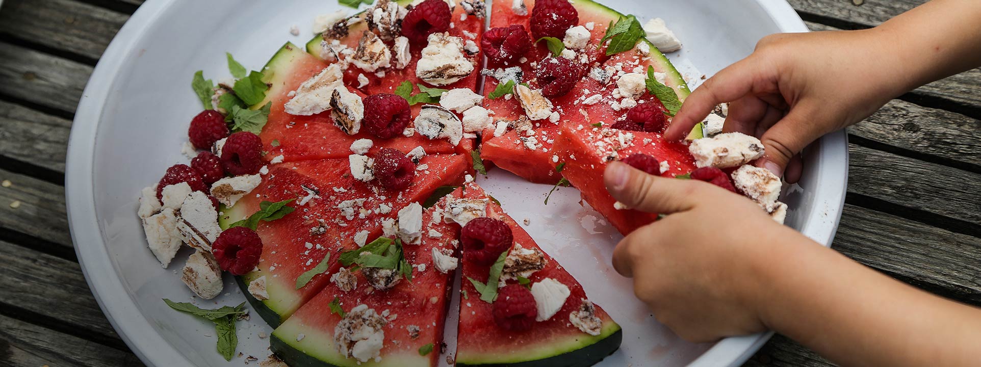 Barnhänder tar en bit vattenmelon med maräng på 