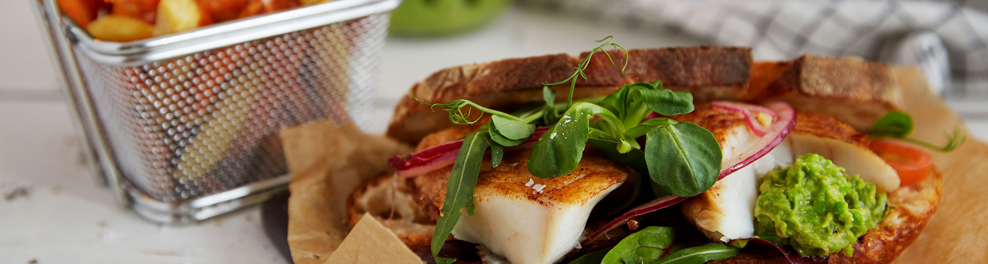 Halstrad torskrygg i rostat bröd på en bädd av krispig örtsallad och ärtguacamole, skivad tomat samt picklad rödlök